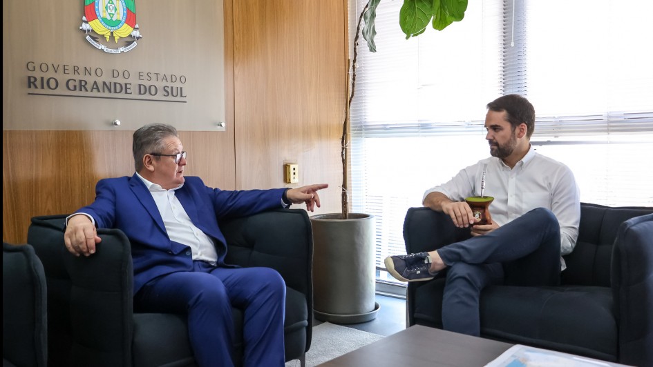 Foto mostra Ranolfo Vieira J&uacute;nior e o governador Eduardo Leite em uma sala. Eles est&atilde;o em poltronas pretas. Ao fundo, um painel com o bras&atilde;o do governo do Estado.