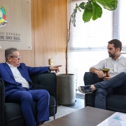 Foto mostra Ranolfo Vieira J&uacute;nior e o governador Eduardo Leite em uma sala. Eles est&atilde;o em poltronas pretas. Ao fundo, um painel com o bras&atilde;o do governo do Estado.