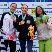 Foto mostra atleta Emanueli Maiara Hein, ao centro, com outras duas atletas. Elas mostram suas medalhas. Ela est&aacute; com um abrigo esportivo preto com o dizer Times RS.