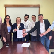 Foto mostra secret&aacute;ria e representantes do hospital exibindo o documento assinado.